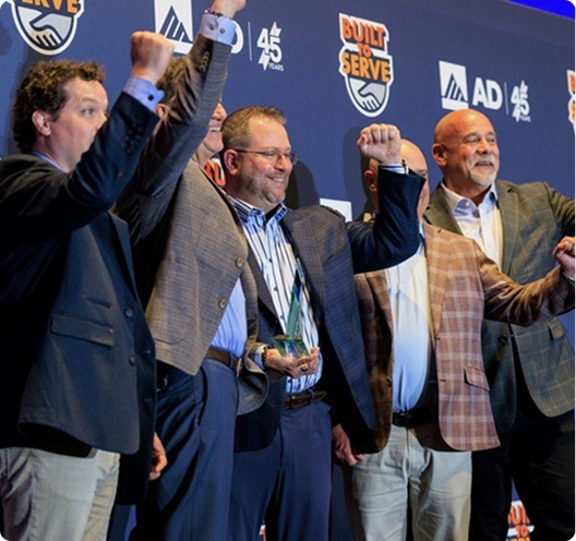 Merit Brass team members celebrating on stage after receiving the 2026 AD PVF Supplier of the Year award